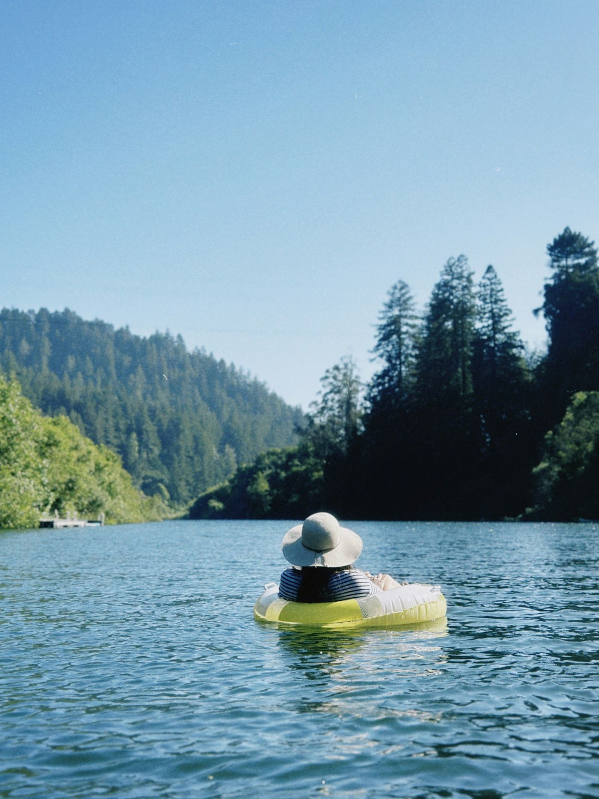 Someone floating on a yellow tube down a forested river