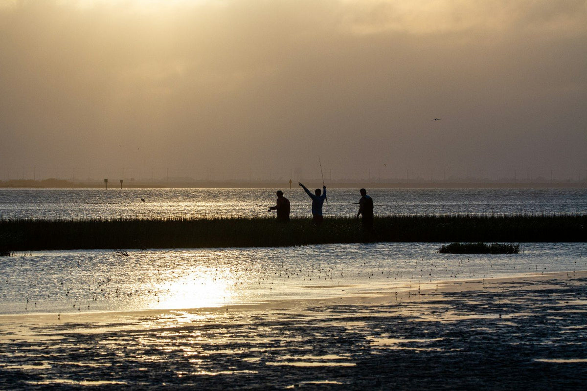 Three people wade fishing at sunset on the Laguna Madre