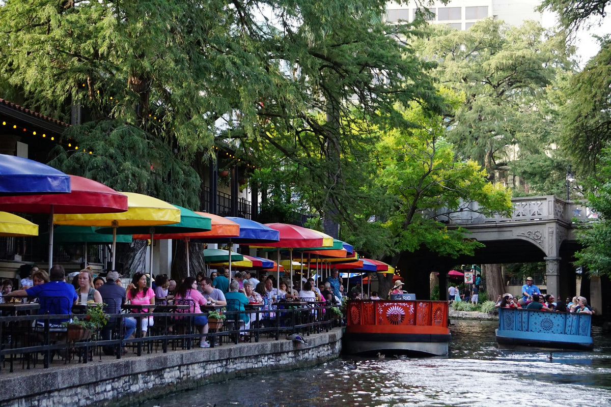 Diners under bright umbrellas on the San Antonio River Walk